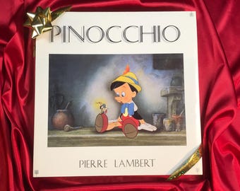 Può includere: Una stampa vintage di Pinocchio, con il titolo in alto e il nome dell'artista, Pierre Lambert, in basso. L'illustrazione raffigura Pinocchio con un piccolo personaggio simile a un insetto. Lo sfondo è una scena interna attenuata.