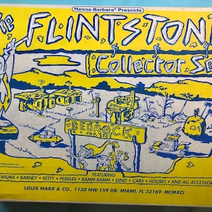 Puede incluir: Caja de coleccionista vintage de los Picapiedra con gráficos amarillos y azules. La caja presenta a Pedro Picapiedra, la ciudad de Bedrock y el texto "The Flintstones Collector Set". Incluye el texto "Featuring Fred, Wilma, Barney, Betty, Pebbles, Bamm Bamm, Dino, Cars, Houses, and All Accessories."