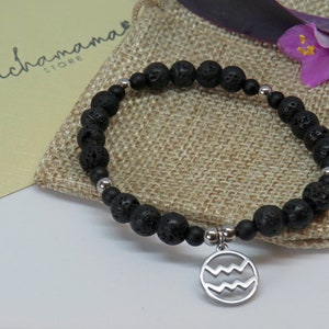 May include: Black lava rock bead bracelet with a silver-tone Aquarius charm. The bracelet features round, porous beads and smaller black and silver beads. The charm displays the Aquarius symbol. The bracelet is displayed on a burlap pouch.