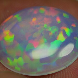 May include: A round, white opal gemstone with a rainbow of colors, including green, pink, and yellow.