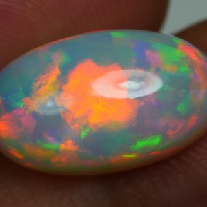 Puede incluir: Una piedra preciosa de ópalo blanco con un juego de colores naranja, verde y morado brillante.