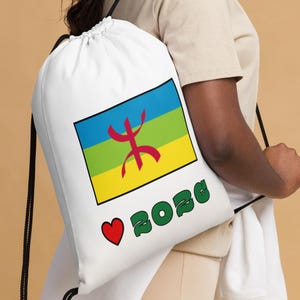 May include: White drawstring backpack featuring a colorful flag design with a red symbol and the text "BOZG" in green. A red heart is next to the text. The bag has black drawstrings.