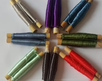 May include: Assortment of ten spools of thread in various colors, including green, red, blue, purple, and gray. Each spool is wrapped in two strands of thread and has a wooden base.