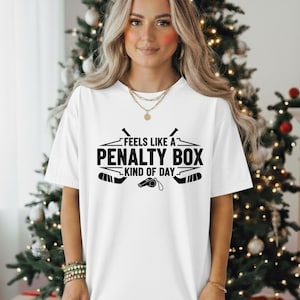 Könnte beinhalten: Weißes T-Shirt mit dem schwarzen Text "Feels Like A Penalty Box Kind of Day". Das Design beinhaltet Hockeyschläger und eine Pfeife. Ein lässiger Unisex-Stil.