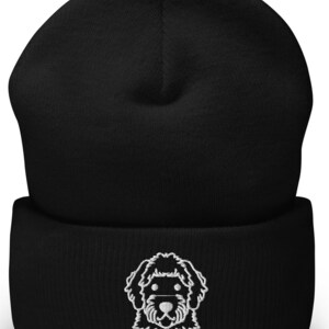 Puede incluir: Gorro negro con un doodle blanco bordado de la cara de un perro.
