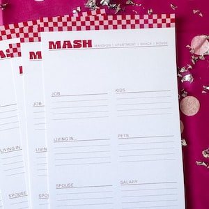 Puede incluir: Una hoja de papel blanca con un borde rojo y blanco a cuadros. El papel tiene la palabra "MASH" impresa en letras negras en la parte superior. Debajo de la palabra "MASH" está el texto "MANSION | APARTMENT | SHACK | HOUSE". El papel está dividido en columnas con encabezados para "JOB", "KIDS", "LIVING IN", "PETS", "SPOUSE", "SALARY", "SPOUSE'S JOB", y "CAR".
