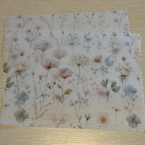 May include: Two sheets of paper with a floral design. The design features watercolor-style flowers in shades of pink, blue, and yellow, with green leaves and stems. The background is a light beige.
