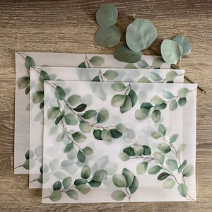 May include: Three sheets of translucent paper with a watercolor eucalyptus leaf pattern. The leaves are green and white on a white background.
