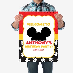 May include: A red, yellow, and black welcome sign with white polka dots. The sign features a black silhouette of Mickey Mouse's head and the text "Welcome to Anthony's Birthday Party! July 31, 2019".