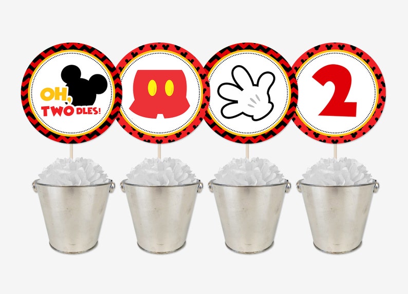 May include: Four red, yellow, and black circular Mickey Mouse themed party decorations with a white background. The decorations feature Mickey Mouse's head, shorts, hand, and the number 2. The decorations are on sticks and placed in silver buckets with white tissue paper.