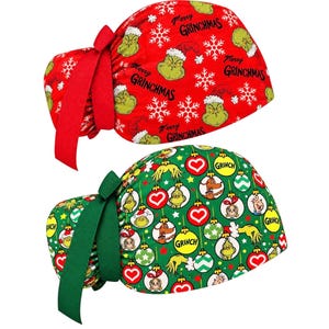 May include: Two scrub caps with tie-back closures. The top cap is red with white snowflakes and green Grinch faces, featuring the text Merry Grinchmas. The bottom cap is green with a pattern of colorful Christmas ornaments containing Grinch characters.