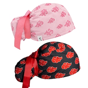 May include: Two scrub caps featuring a repeating cloud pattern. One cap is light pink with darker pink clouds and a pink ribbon tie. The other cap is black with red clouds and a red ribbon tie. Both caps have a gathered back and a small white label.