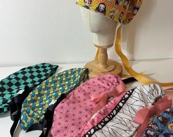 May include: A collection of scrub caps featuring various anime-inspired patterns, including a yellow cap with character prints on a mannequin head, and four folded caps in green-black checkerboard, yellow-blue geometric, pink, and white-black designs.
