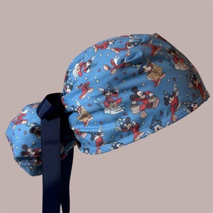 Puede incluir: Un gorro quirúrgico azul con un patrón repetitivo de Mickey Mouse vestido de mago con túnica roja y sombrero azul, intercalado con pequeñas estrellas. El gorro incluye una cinta azul marino en la parte posterior para un ajuste regulable.