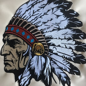 May include: Embroidered patch depicting a Native American man wearing a headdress with blue, white and black feathers. The man has a serious expression and is looking to the left. The headdress has a red and blue band with a gold accent.