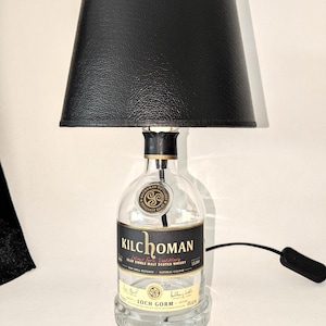 Könnte beinhalten: Ein schwarzer Lampenschirm mit einer klaren Glasflaschenbasis. Die Flasche ist mit "Kilchoman" und "Isle for Islay Single Malt Scotch Whisky" beschriftet.