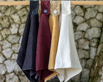 May include: Four kitchen towels hanging on a wooden rod. The towels are black, burgundy, beige, and white. Each towel has a different patterned fabric trim.