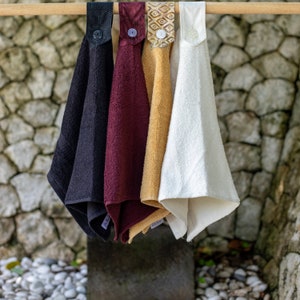 May include: Four kitchen towels hanging on a wooden rod. The towels are black, burgundy, beige, and white. Each towel has a different patterned fabric trim.