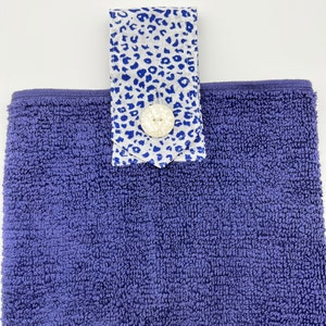 May include: A purple terry cloth hand towel with a white and blue patterned fabric loop and a white button.