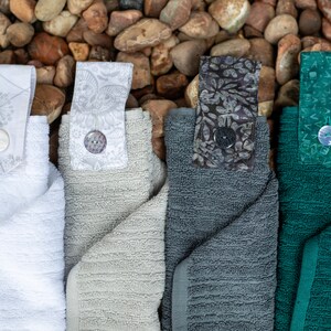 May include: Four kitchen towels with different colored fabric and patterned fabric loops. The towels are white, gray, dark gray, and green.