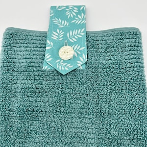 May include: A teal blue kitchen towel with a white button and a teal blue and white patterned fabric loop.