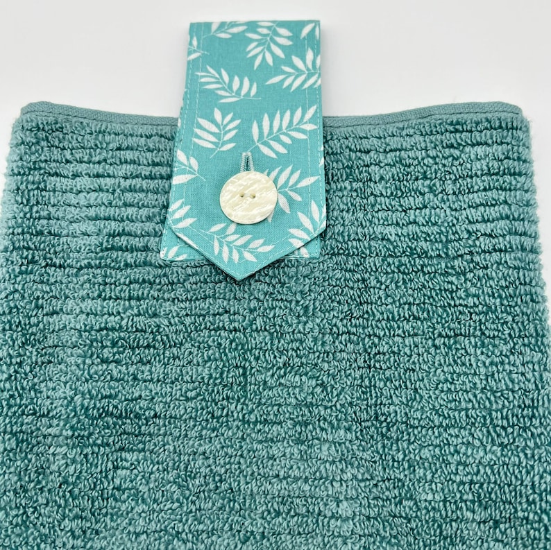 May include: A teal blue kitchen towel with a white button and a teal blue and white patterned fabric loop.