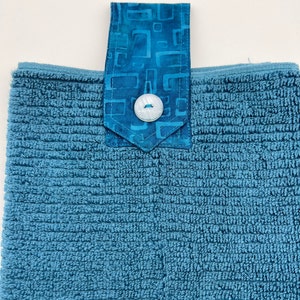 May include: A blue terry cloth kitchen towel with a blue and white patterned fabric loop and a white button.