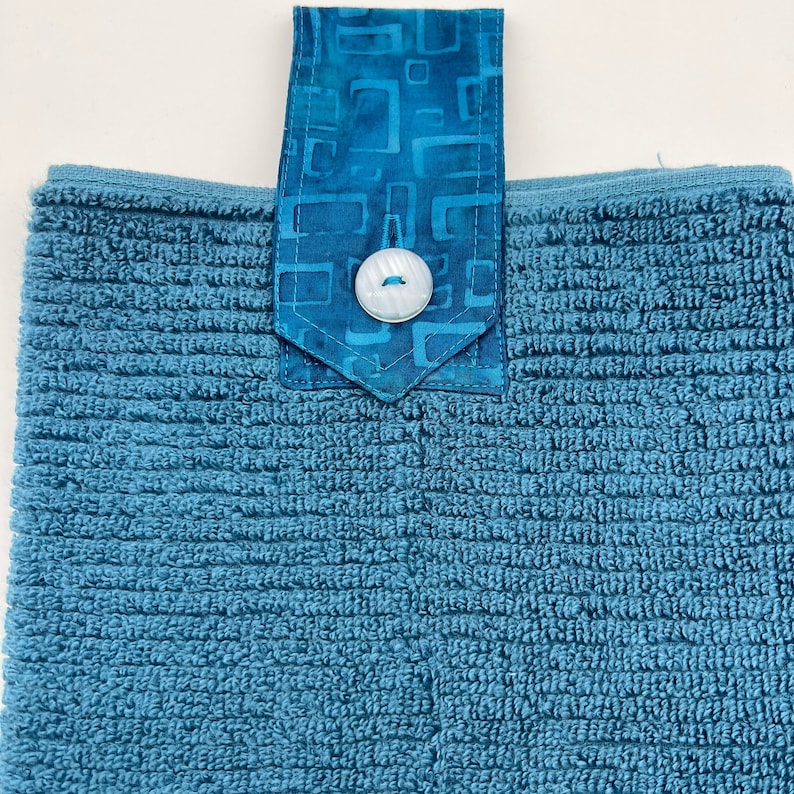 May include: A blue terry cloth kitchen towel with a blue and white patterned fabric loop and a white button.