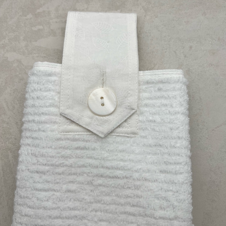 May include: White kitchen towel with a white button and a white fabric loop. The towel has a textured, ribbed surface.