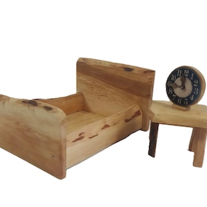 May include: A miniature wooden bed frame and nightstand set. The bed frame is light brown with a natural wood grain. A small, round clock with a black face and white numbers sits on the nightstand.