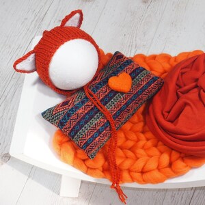 Könnte beinhalten: Eine gestrickte orangefarbene Fuchsmütze mit weißen Innenohren sitzt auf einem weißen Schaumstoffkopf. Ein gemustertes Kissen mit einem orangefarbenen Herz und ein gerollter orangefarbener Stoff liegen auf einer orangefarbenen Strickdecke. Der Text "SET #3" befindet sich oben rechts.