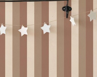 May include: A kitchen with a brown and white striped wallpaper. A white shelf with a clock, a wooden box, and two glass bottles. A string of white stars hangs from the shelf. A wooden countertop with a black wire rack, a glass jar with oats, a white pitcher, a stack of white plates, and two clear glasses.