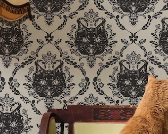 May include: An orange tabby cat stands on its hind legs, reaching towards a patterned wallpaper. The wallpaper features a repeating design of black cat faces within a floral damask pattern. A vintage floor lamp and a green chair are also in the scene.