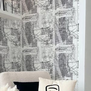 Könnte beinhalten: Ein gemütliches Wohnzimmer mit einem cremefarbenen Sessel, einem schwarzen Kissen und einem Kissen mit Gesichtszeichnung. Eine schwarze Vase hält Pampasgras. Ein kleiner schwarzer Beistelltisch und ein gerahmtes Kunstwerk vervollständigen die Einrichtung.