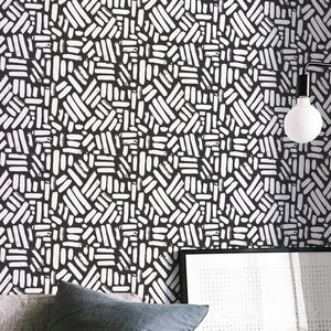 Puede incluir: Una sala de estar con un sofá gris, una mesa de café de madera, una silla blanca y un papel tapiz estampado en blanco y negro. Una revista está sobre la mesa de café.