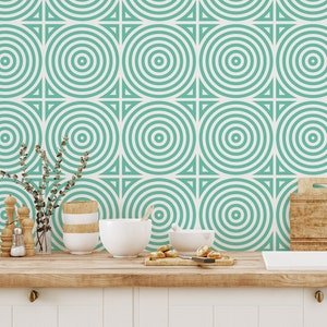 May include: A kitchen with a teal and white geometric patterned wallpaper. The wallpaper features a repeating pattern of concentric circles. The kitchen has a white countertop, a white sink, and a gold faucet.
