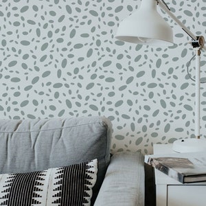 May include: A grey sofa with a black and white patterned cushion sits in front of a wall with a grey and white abstract pattern. A white lamp with a white shade sits on a white side table next to the sofa.