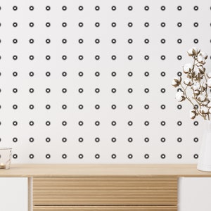 May include: A white ceramic pitcher with a cotton flower bouquet on a wooden shelf with a white background. The background has a repeating pattern of black circles.