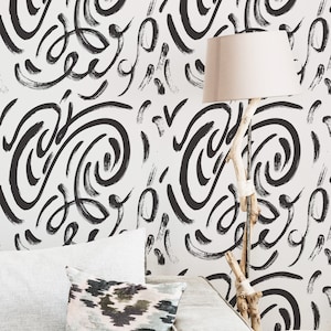 Puede incluir: Un sofá blanco con un cojín estampado en blanco y negro. La pared detrás del sofá está cubierta con un papel tapiz abstracto en blanco y negro con un diseño de pinceladas.