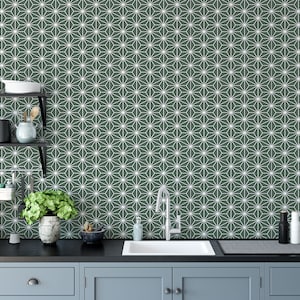 May include: A kitchen with a dark green tiled backsplash featuring a white geometric pattern. The backsplash is behind a black countertop with a stainless steel sink and faucet. There are two cabinets below the countertop.