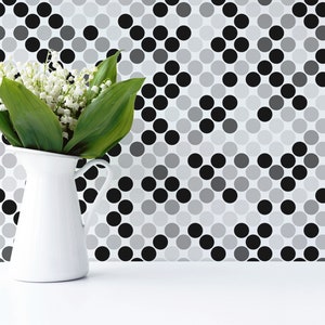 May include: A white ceramic pitcher with a bouquet of white lily of the valley flowers in front of a black and white geometric patterned wall.