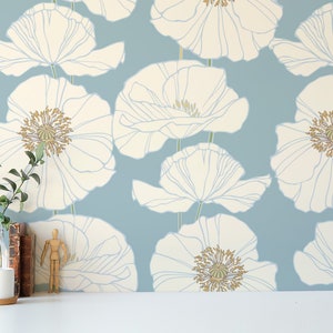 May include: A blue and white floral wallpaper with a white poppy flower pattern. The wallpaper is displayed on a wall with a small plant, a mug, and a wooden figurine on a white surface.