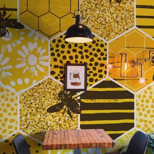 May include: A cafe interior with a yellow and white honeycomb patterned wall, featuring bee silhouettes and a framed picture. A wooden table and two black chairs are in front of the wall. A black pendant light hangs above the table.