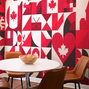 Puede incluir: Un comedor con una mesa blanca, sillas de cuero marrón y una pared cubierta con un patrón geométrico rojo, blanco y negro con símbolos canadienses. Un cuenco de madera con fruta está sobre la mesa.
