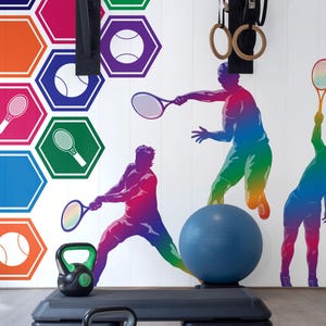 Può includere: Una palestra domestica con una parete bianca che presenta un design colorato a tema tennis. La parete ha una sbarra per trazioni, anelli da ginnastica e una silhouette di un giocatore di tennis. Sul pavimento ci sono due kettlebell neri, una palla da esercizi blu e una piattaforma di step nera.
