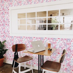 Pink Watercolor Botanical peel and stick wallpaper shows a soft floral look covering the wall behind a small table.