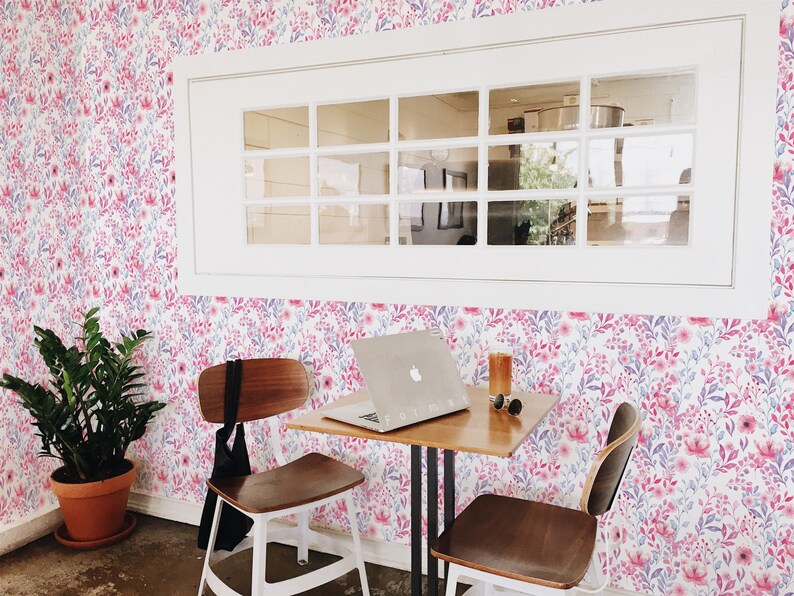 Pink Watercolor Botanical peel and stick wallpaper shows a soft floral look covering the wall behind a small table.