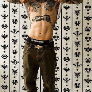 May include: Olive green cargo pants with large side pockets, a black belt with a Dsquared logo buckle, and a silver chain. The pants are paired with black Supreme branded underwear and orange and white sneakers. The garment features a loose fit.