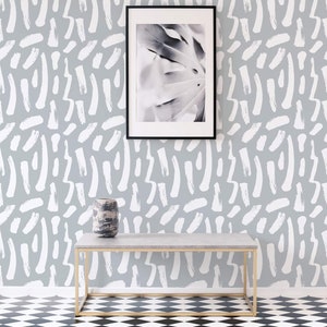 May include: A gray and white wallpaper with a white abstract brushstroke pattern. A black picture frame with a black and white photo of a leaf is hanging on the wall. A gray table with a gray vase is in front of the wall.