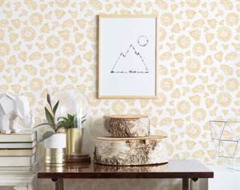 Puede incluir: Una lámina enmarcada con un dibujo lineal negro de una montaña y un círculo, sobre una pared blanca con estampado floral amarillo. La escena incluye una figura de elefante blanca, libros, una planta en maceta dorada y troncos.